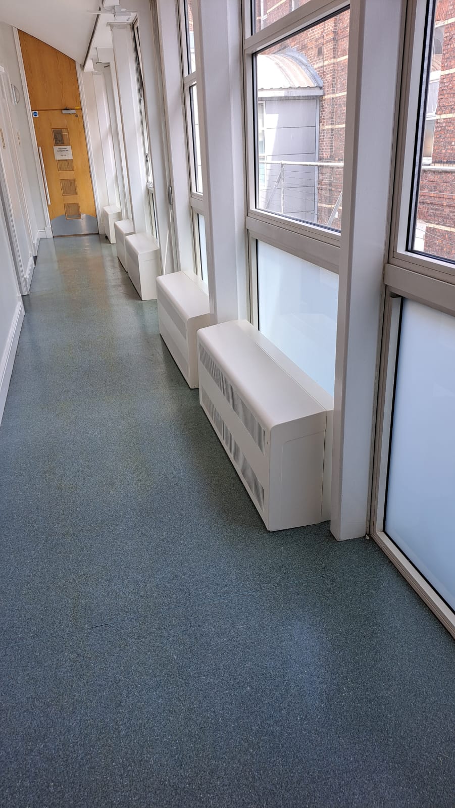 White Eazi-Access radiator covers with bespoke back panels alongside a glazed hospital corridor wall
