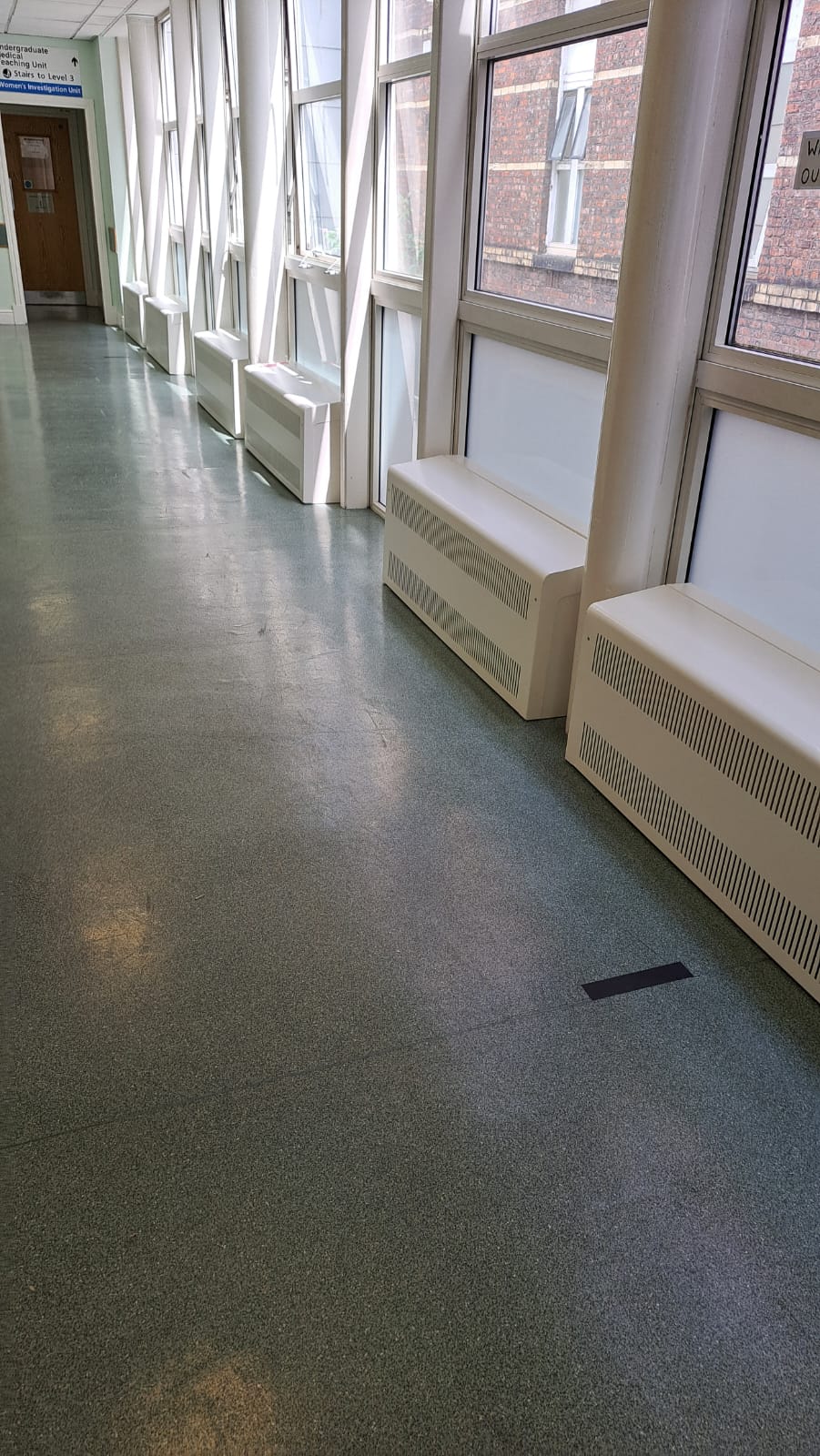 A row of slotted steel radiator covers fitted between the glazing frames in a hospital corridor